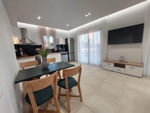 Uma cozinha moderna com área de jantar, televisão de tela plana e uma grande janela com cortinas.