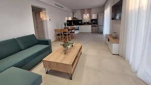 A modern living room with a sofa, coffee table, and dining area. A kitchen is visible in the background. - Villa Luna 1 with swimming pool in Pitsidia (Pitsidia)