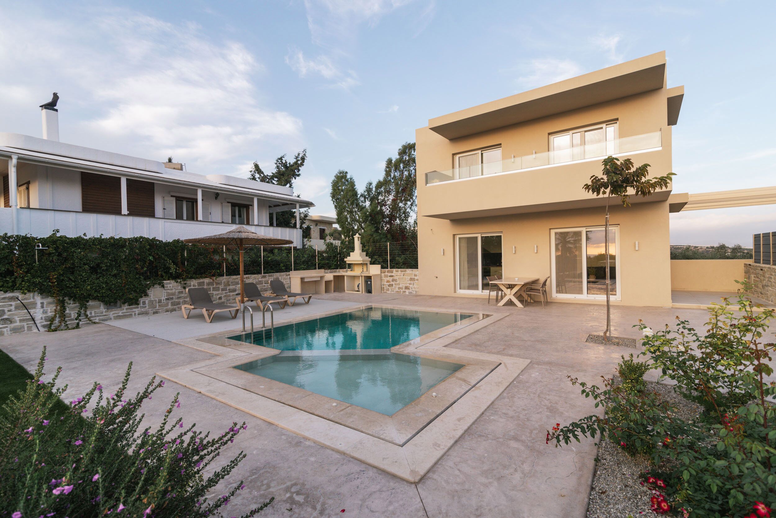 A modern two-story house with a swimming pool, outdoor seating, and a stone wall.