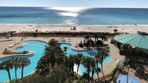 A pool area with palm trees, a beach, and a clear view of the ocean.