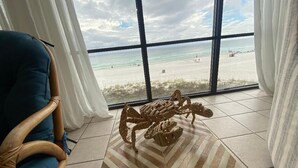 A room with a large window overlooking a beach, a wooden chair, and a patterned rug.