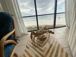 A room with a large window overlooking a beach, a wooden chair, and a patterned rug.