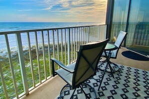 Un balcon avec deux chaises et une table, donnant sur une plage et l’océan.