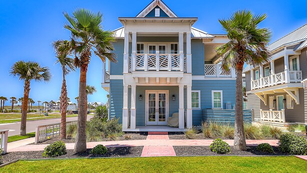 A two-story house with a balcony, surrounded by palm trees and a well-maintained lawn.