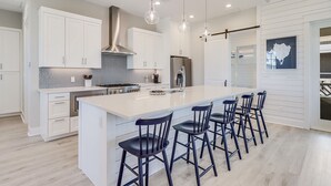 A modern kitchen with white cabinetry, a large island with bar stools, and pendant lighting.