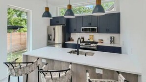 Une cuisine moderne avec des meubles de couleur sombre, des appareils en acier inoxydable et des luminaires suspendus.