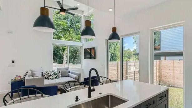 Une cuisine moderne dotée d’un îlot central, de luminaires suspendus et donnant sur le jardin arrière.