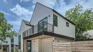 Une maison moderne à deux étages, dotée d’un garage, d’un balcon et d’une clôture en bois.