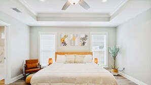 A bedroom with a large bed, a wooden headboard, two wall-mounted lamps, a potted plant, and artwork on the wall. - Luxury New Tranquil Retreat-Walk to Waterfront (Ocean Springs)