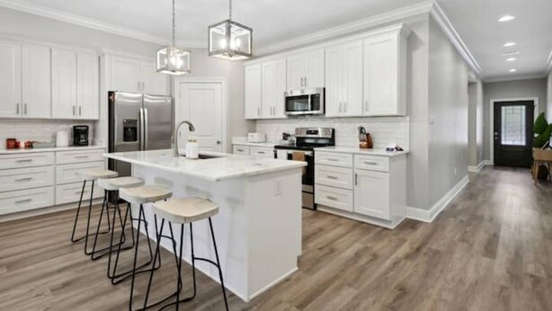 A modern kitchen with white cabinetry, a central island with stools, stainless steel appliances, and a pendant light. - Luxury New Tranquil Retreat-Walk to Waterfront (Ocean Springs)