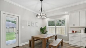 A modern kitchen with white cabinets, a wooden dining table, and a bench. - Luxury New Tranquil Retreat-Walk to Waterfront (Ocean Springs)