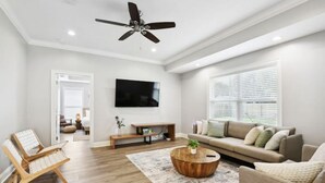 A modern living room with a ceiling fan, a flat-screen TV, a beige sofa, a wooden coffee table, and a patterned rug. - Luxury New Tranquil Retreat-Walk to Waterfront (Ocean Springs)