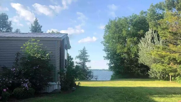 Une maison avec vue sur un lac, entourée d’arbres et bordée d’une pelouse.