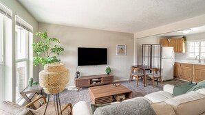A living room with a flat-screen TV, a coffee table, a sofa, and a dining area with a table and chairs. - NO exta fees, Beautiful half duplex 3br, 2ba, w/gym, office and fenced in yard. (Aurora)