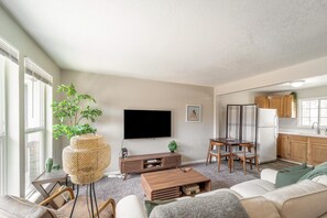 A living room with a flat-screen TV, a coffee table, a sofa, and a dining area with a table and chairs. - NO exta fees, Beautiful half duplex 3br, 2ba, w/gym, office and fenced in yard. (Aurora)