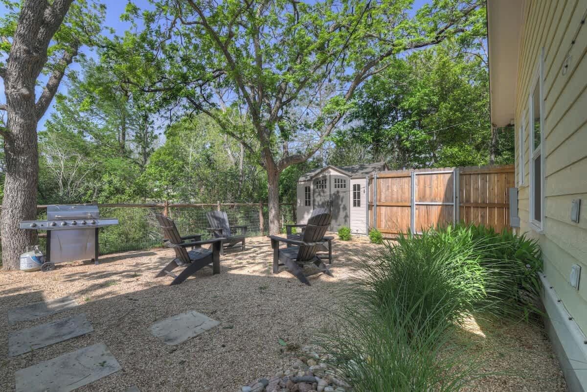 A backyard with a barbecue grill, two chairs, and a wooden fence.