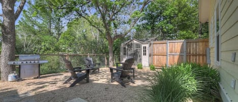 A backyard with a barbecue grill, two chairs, and a wooden fence.