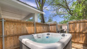 Un jacuzzi en un patio trasero con vallas de madera y un porche cubierto.