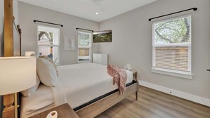Un dormitorio con cama, mesitas de noche, lámpara y ventanas con persianas.