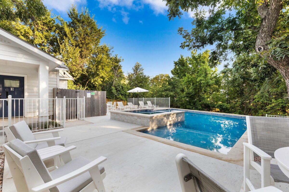Une piscine avec des chaises longues, un espace de détente couvert et une clôture en bois.
