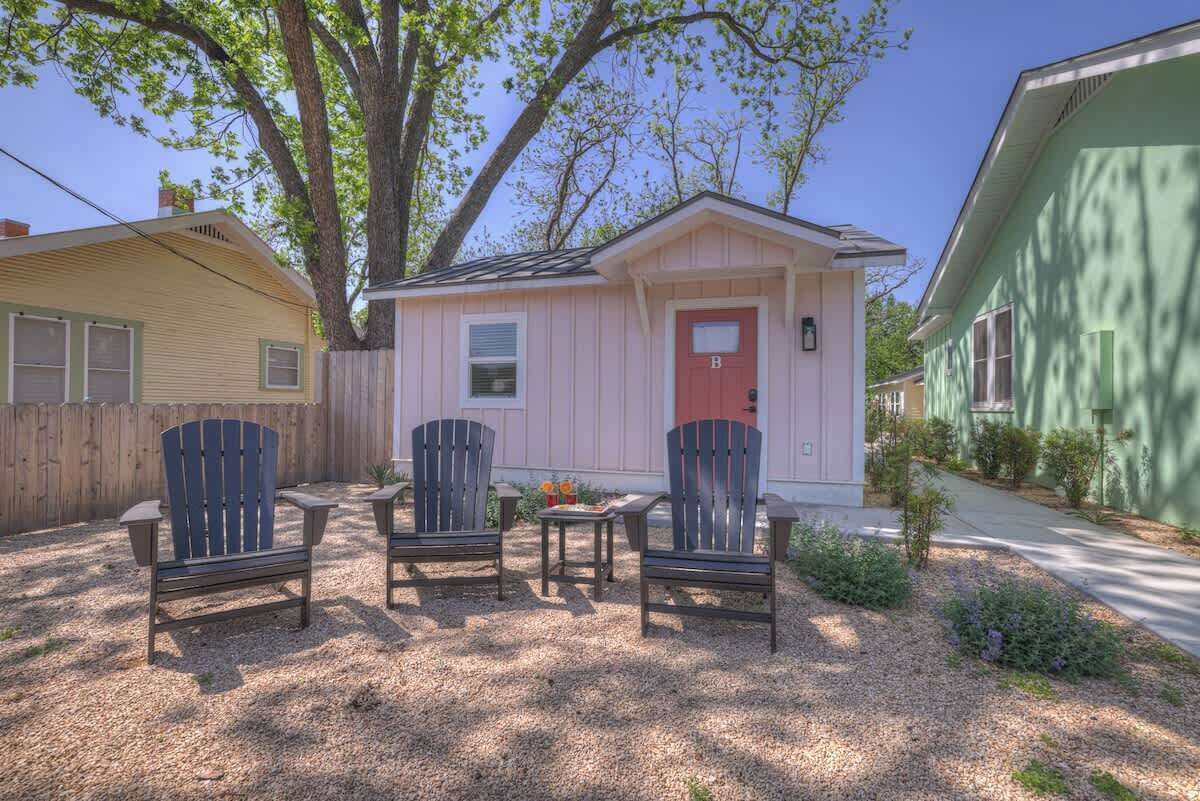A small pink house with a red door, two Adirondack chairs, and a table in front.