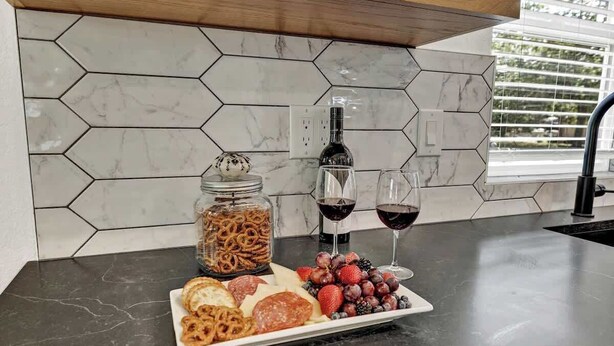 Un piano di lavoro in cucina con zellige esagonali, una bottiglia di vino, due calici di vino, un piatto di stuzzichini e un barattolo di grissini.