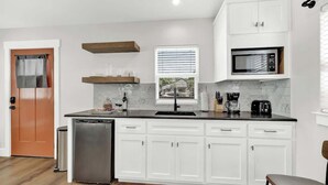 Una cucina moderna con mobili bianchi, un piano di lavoro nero, un forno a microonde integrato e una finestra con persiane.