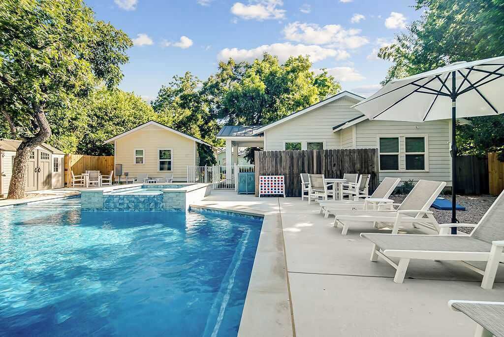 A swimming pool with lounge chairs and umbrellas, surrounded by a wooden fence and trees.