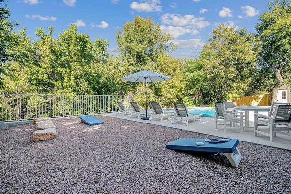 An outdoor pool area with lounge chairs and a table, surrounded by a fence and trees.