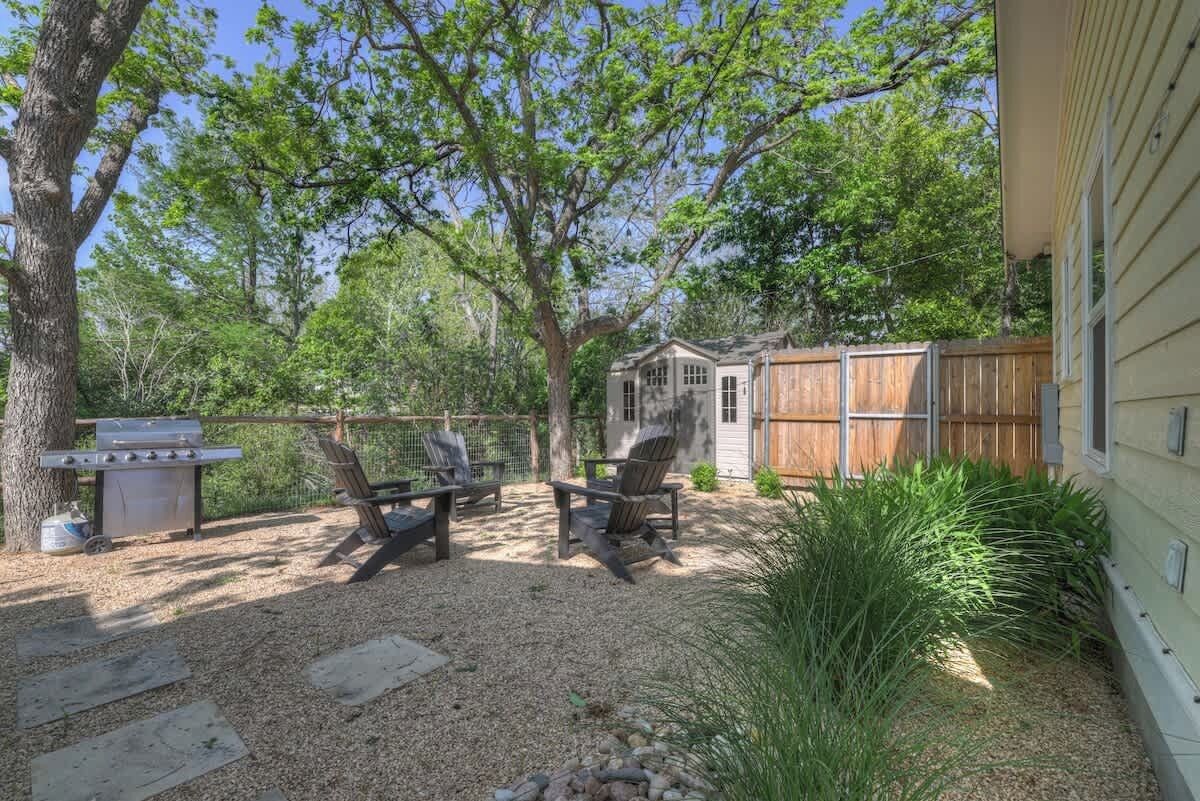 A backyard with a barbecue grill, two wooden chairs, and a wooden fence.