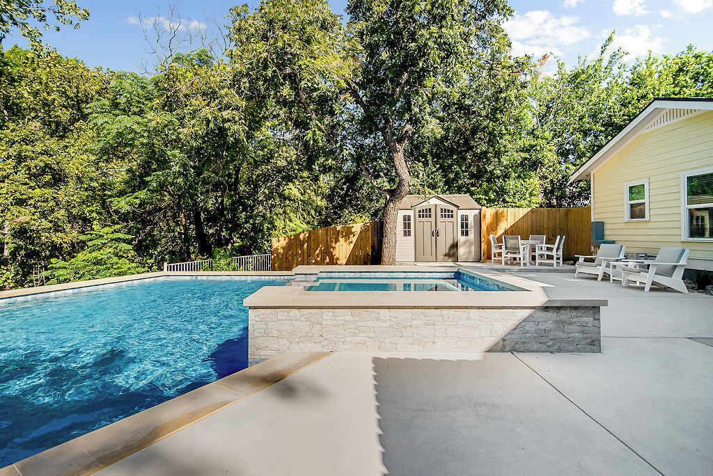 A swimming pool with a stone deck, surrounded by a wooden fence and trees.
