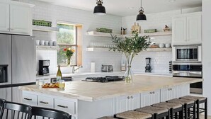 A modern kitchen with white cabinetry, a large island with bar stools, a built-in oven, and pendant lighting. - The Point Serene Hill Country Views With Pool & Hot Tub (Fredericksburg)