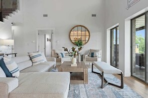 A modern living room with a sectional sofa, a coffee table, and a large round mirror. - The Point Serene Hill Country Views With Pool & Hot Tub (Fredericksburg)