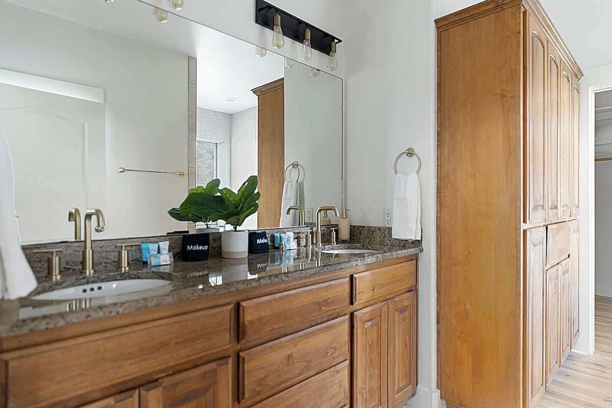 Un baño con tocador de madera, dos lavamanos, un espejo grande y una planta en maceta.