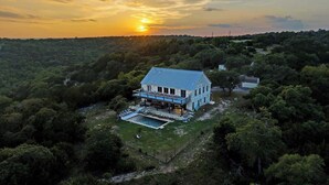 A large house with a swimming pool, surrounded by dense forest. - The Point Serene Hill Country Views With Pool & Hot Tub (Fredericksburg)