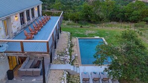 A poolside area with a long bench, a pool, and a view of the surrounding landscape. - The Point Serene Hill Country Views With Pool & Hot Tub (Fredericksburg)