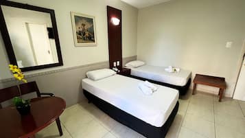 A hotel room with two beds, a desk, a chair, a small table, a mirror, and a painting on the wall.