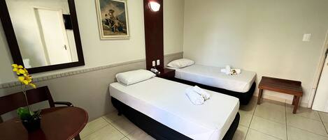 A hotel room with two beds, a desk, a chair, a small table, a mirror, and a painting on the wall.