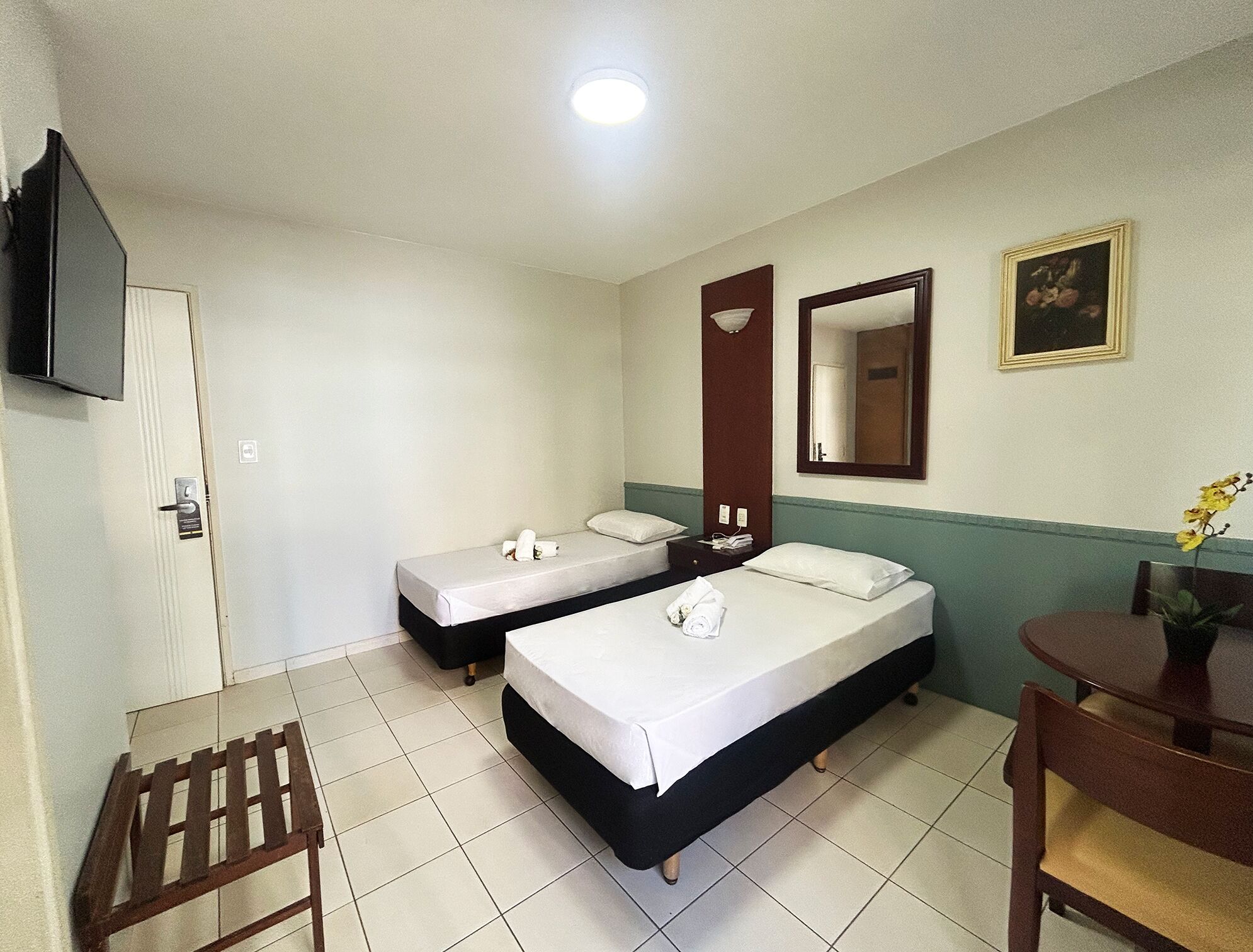 Une chambre d’hôtel avec deux lits simples, un bureau, une chaise, un téléviseur fixé au mur et un miroir au-dessus du bureau.