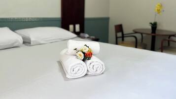Una cama bien hecha con toallas blancas enrolladas y un arreglo floral encima.