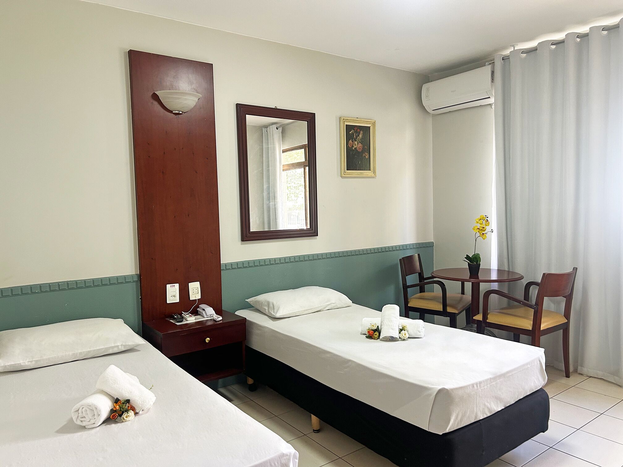 Habitación de hotel con dos camas, un escritorio, una silla, una mesita, un espejo y un equipo de aire acondicionado.