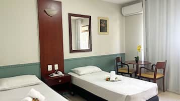 Habitación de hotel con dos camas, un escritorio, una silla, una mesita, un espejo y un equipo de aire acondicionado.