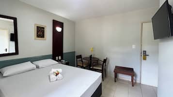 Habitación de hotel con cama, escritorio, silla, mesita, televisor y puerta.