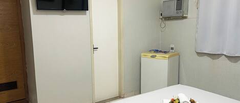 Una habitación de hotel con cama, televisor montado en la pared, equipo de aire acondicionado y armario de madera.
