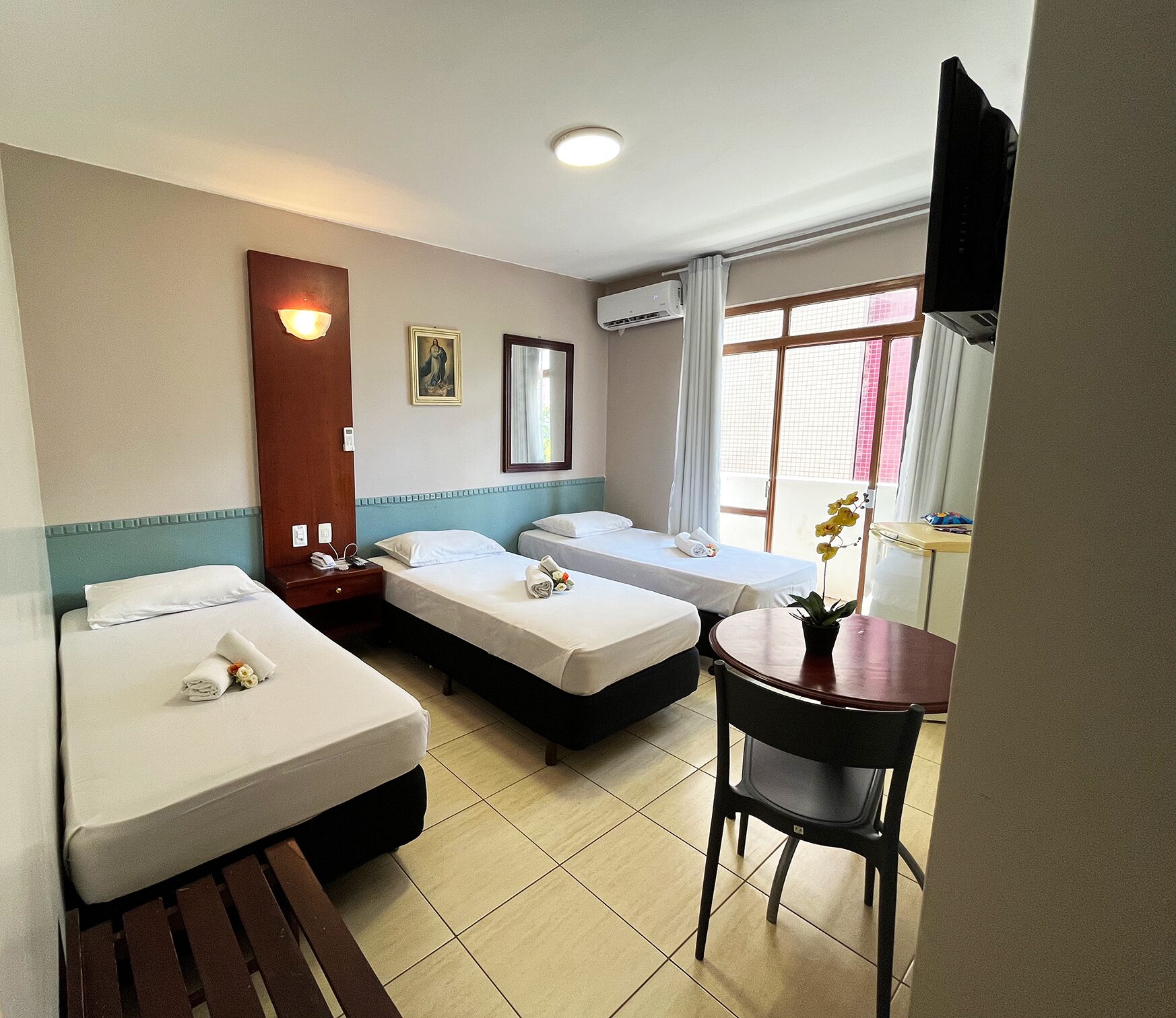 Habitación de hotel con dos camas individuales, una mesita con una silla, televisor y ventana con cortinas.