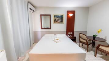 A hotel room with a bed, a bedside table, a chair, a small table with a plant, a mirror, and a picture on the wall.