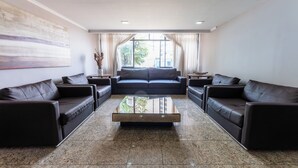A modern living room with a sofa set, a glass coffee table, and a large window with curtains. - Hotel Alvorada by Bsb Inn (Taguatinga)