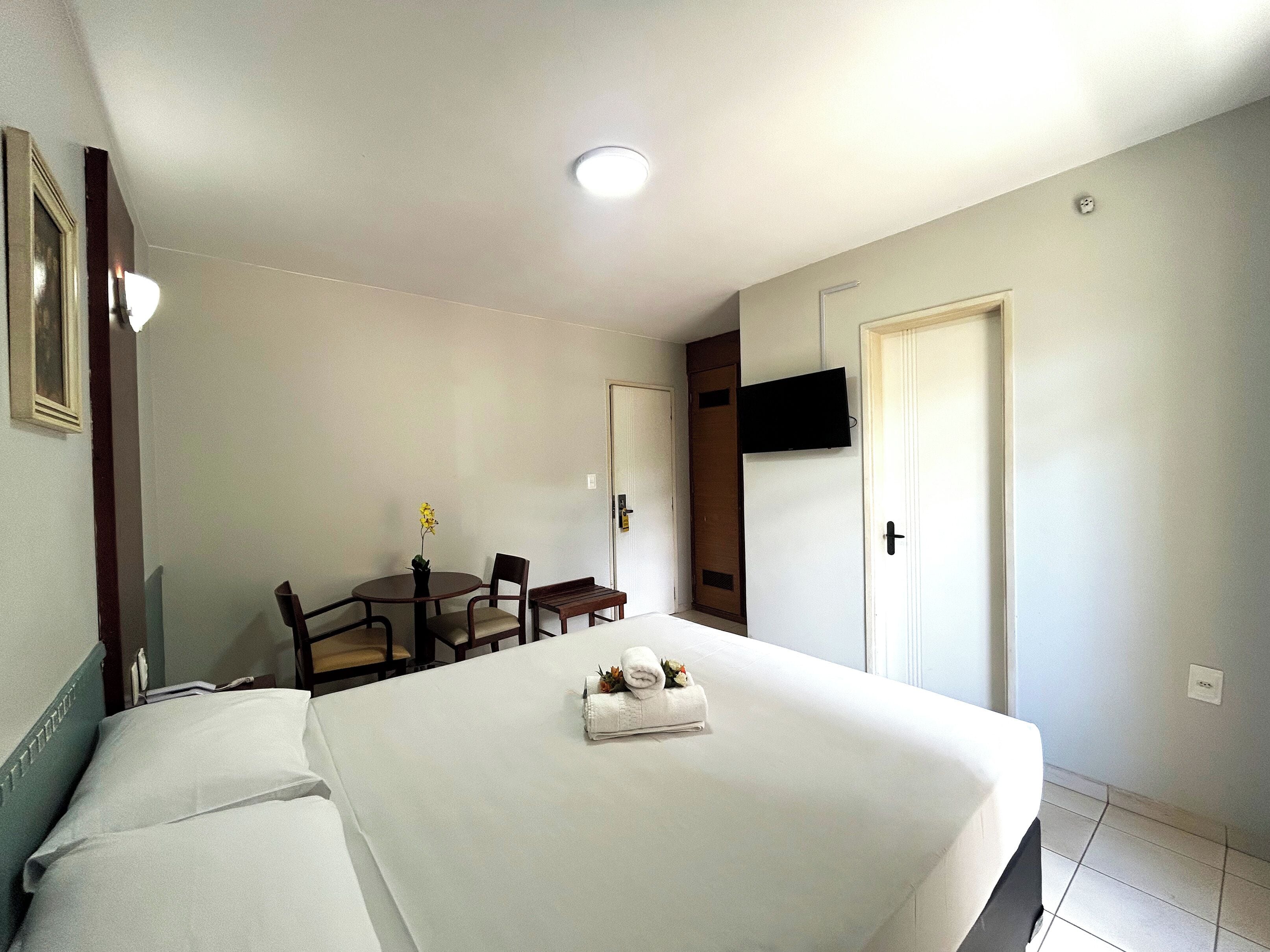 Una habitación de hotel con cama, una pequeña mesa con sillas, un televisor en la pared y una puerta.