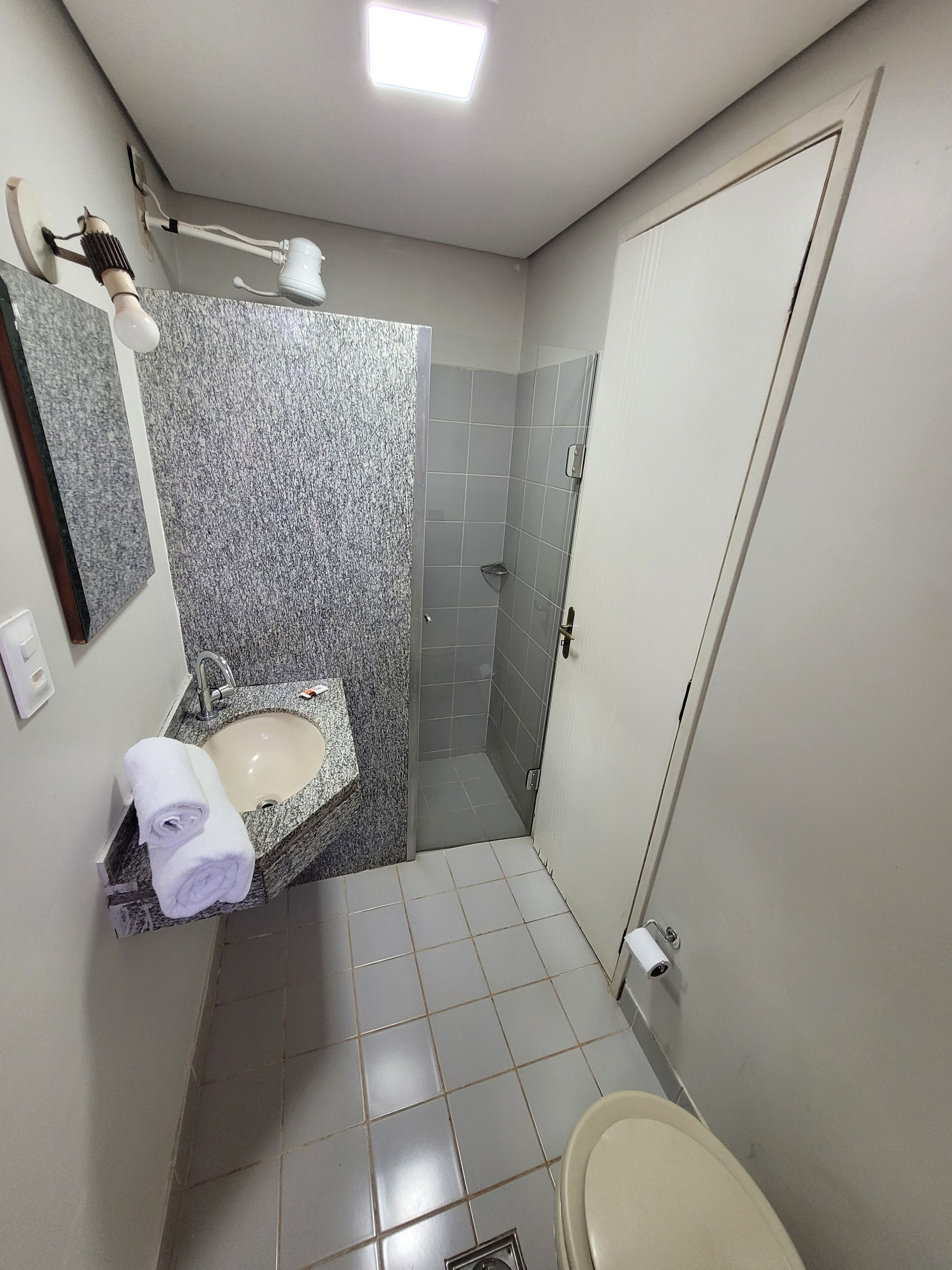 A compact bathroom with a sink, mirror, towel, shower, and toilet.