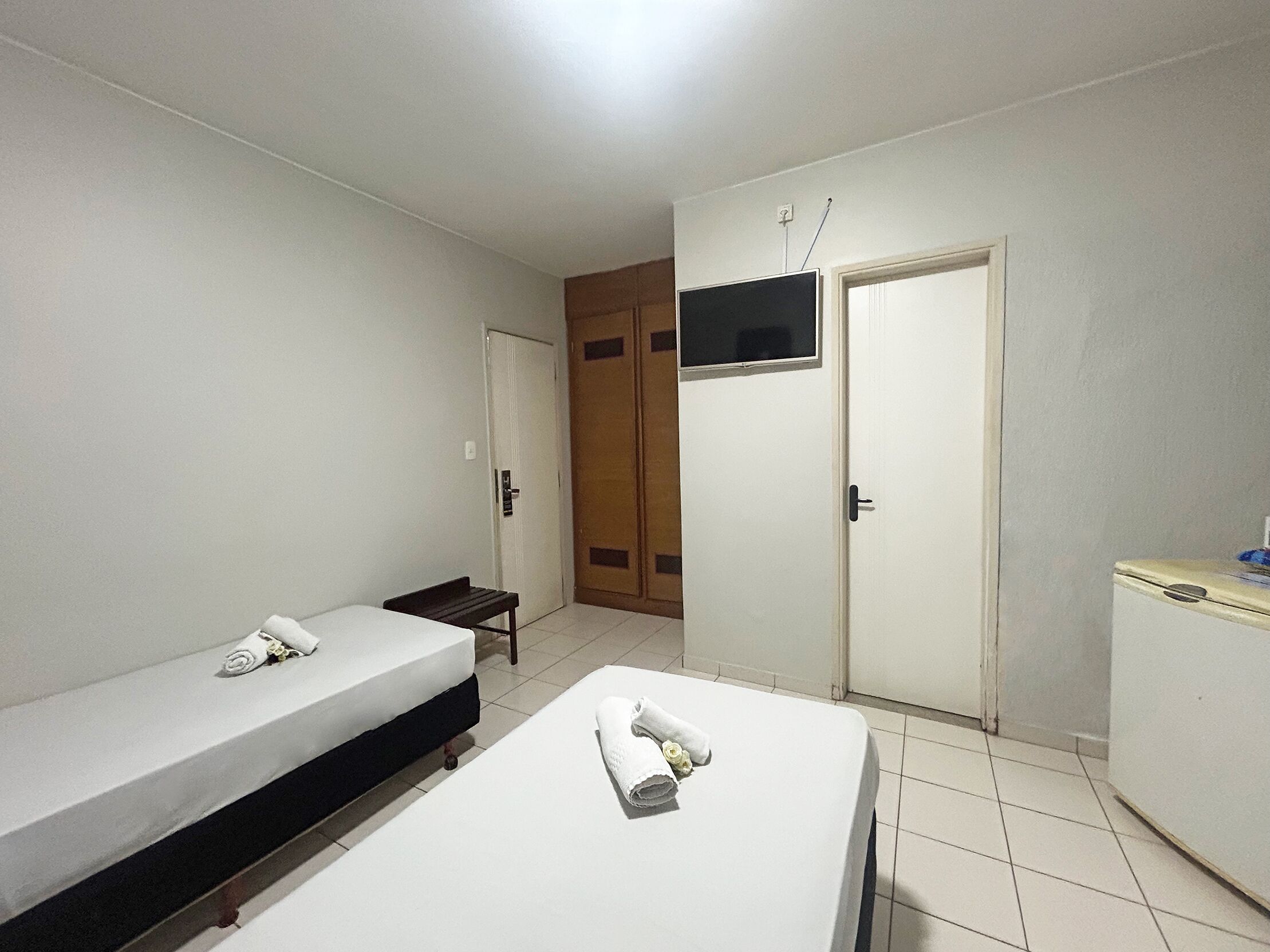 Una habitación pequeña y limpia con dos camas individuales, un televisor montado en la pared y un armario con espejo.